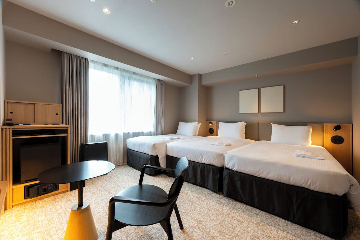 A hotel room with two beds, a TV, a desk, and a chair.