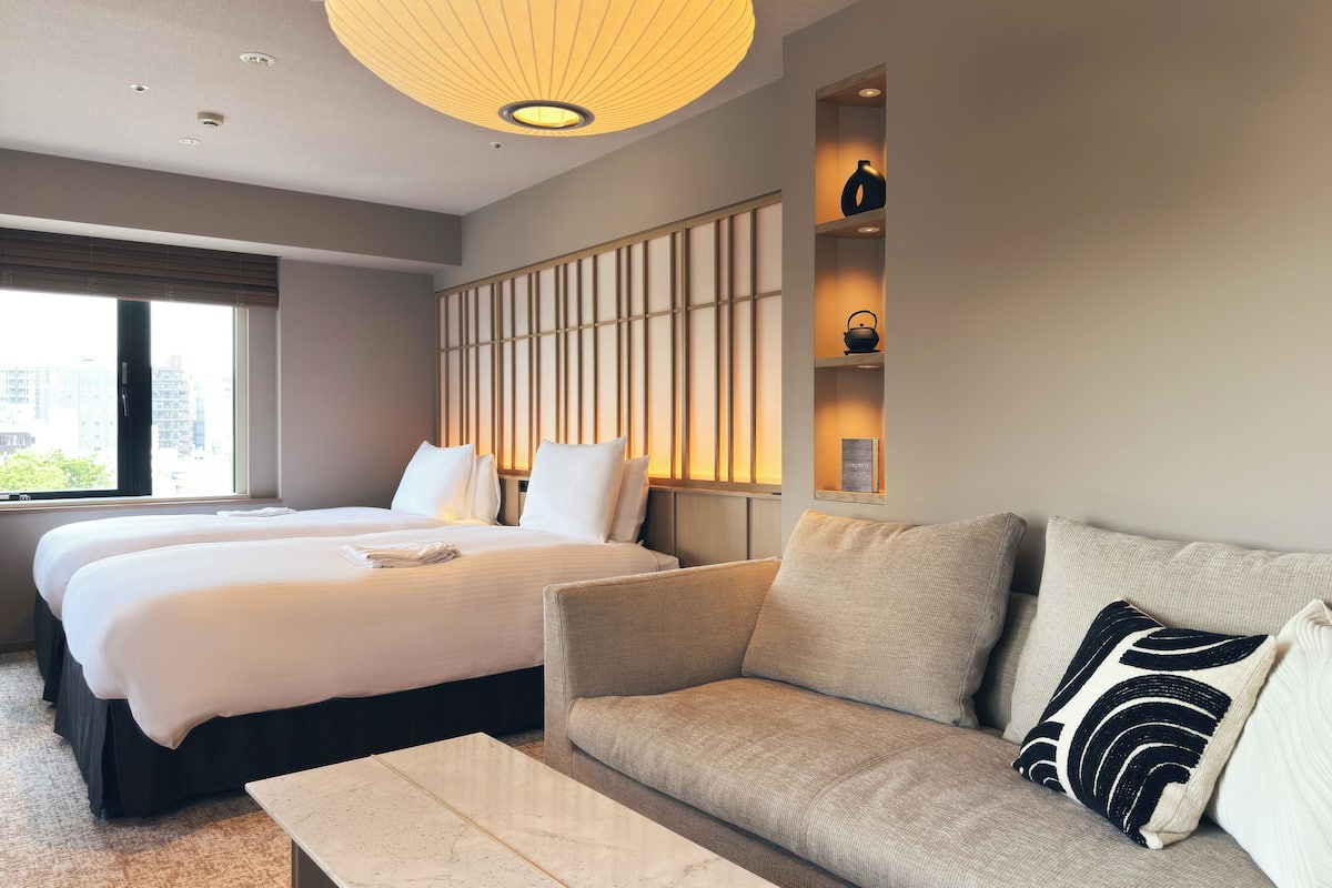 A hotel room with two beds, a sofa, a coffee table, and a wall-mounted shelf with decorative items.