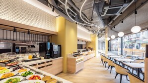 Une cafétéria moderne avec un buffet, un plancher en bois et une vue sur la rue grâce à de grandes fenêtres.