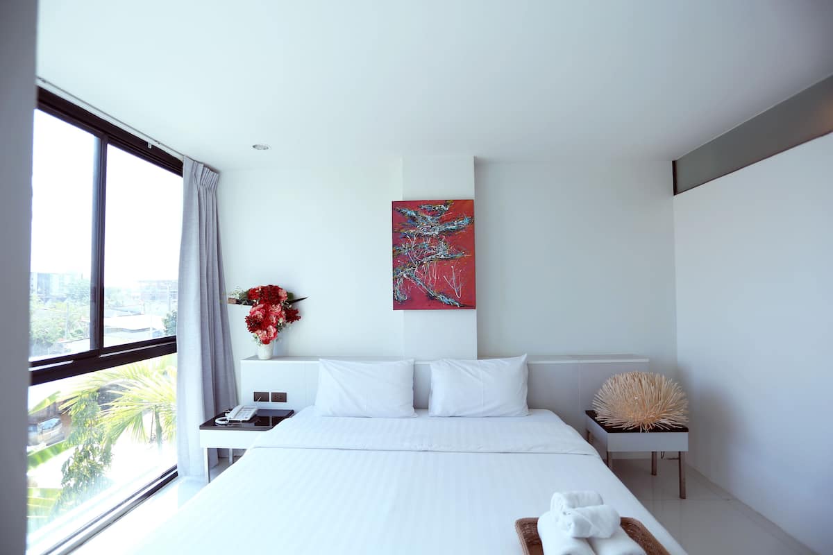Une chambre d’hôtel moderne avec un grand lit, une table de chevet, un vase de fleurs et un tableau au mur.