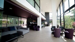 Een moderne lobby met een grijze bank, paarse stoelen en een receptiebalie.