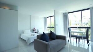 Een moderne hotelkamer met een bed, een bank, een eettafel met stoelen, en grote ramen met uitzicht op de omgeving.