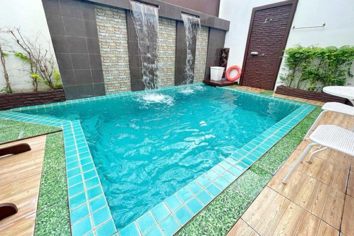 A swimming pool with a waterfall feature, surrounded by a wooden deck and a small patio area.