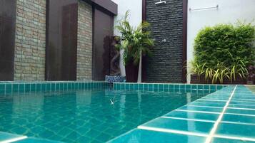 A swimming pool with a tiled edge, a stone wall with a door, and potted plants.