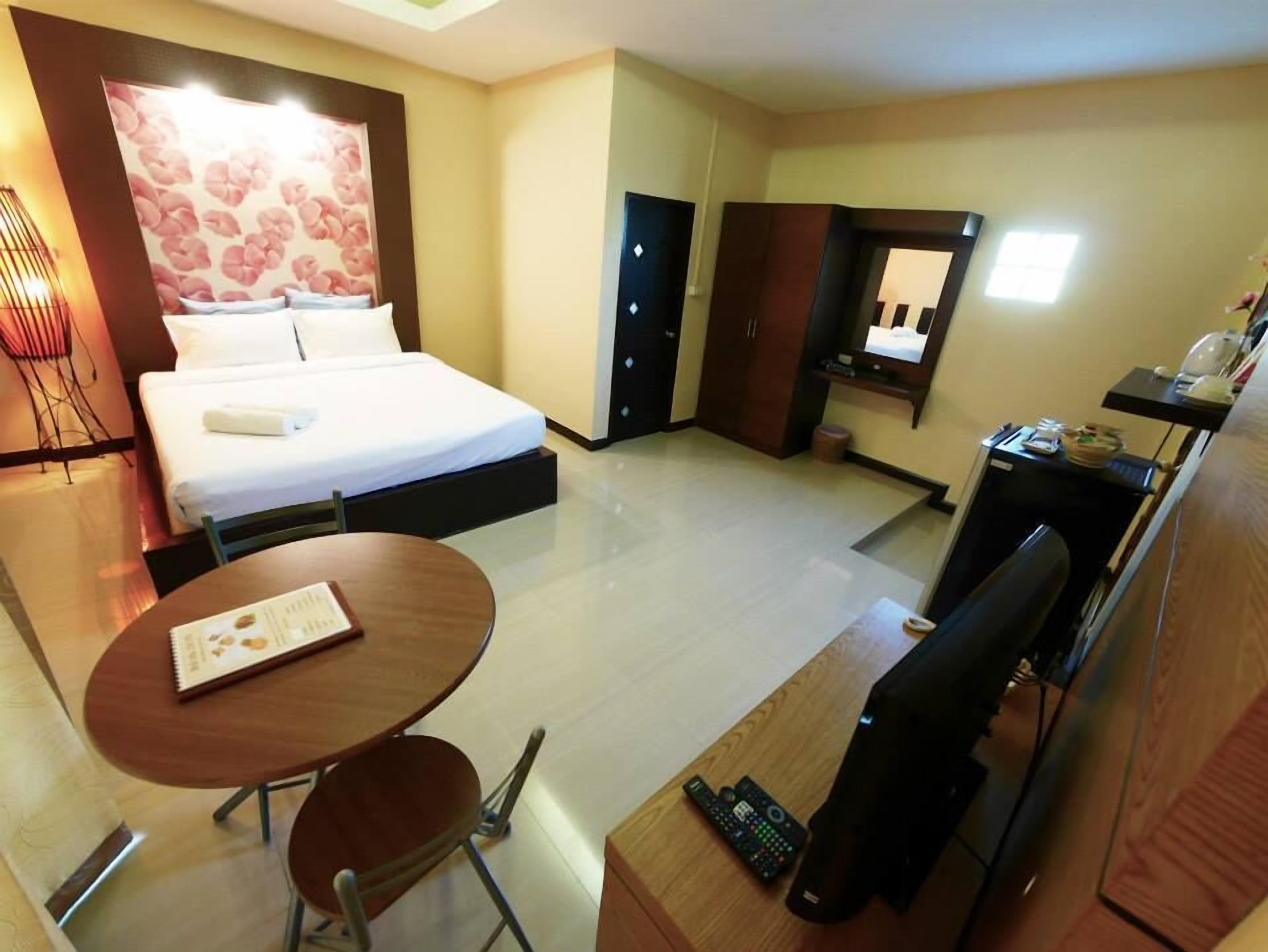 A hotel room with a bed, a desk with a chair, a small table, a TV, and a wardrobe.