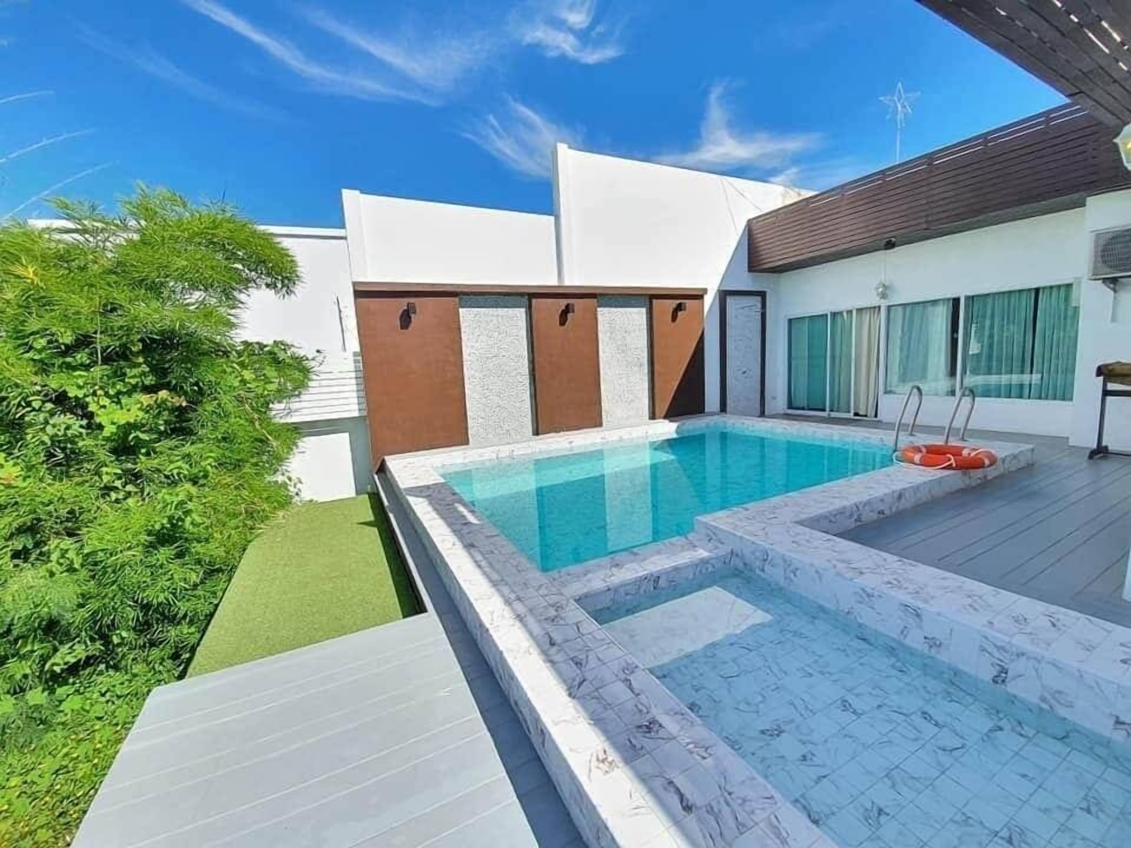 A modern outdoor swimming pool with a clear blue water feature, surrounded by a wooden deck and a small garden area.