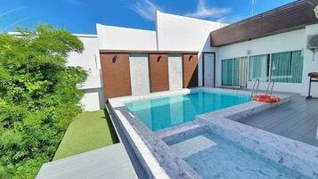A modern outdoor swimming pool with a clear blue water feature, surrounded by a wooden deck and a small garden area.