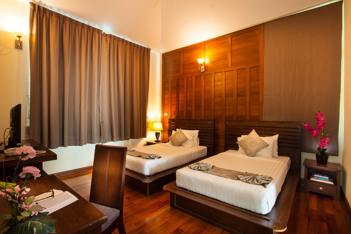 A hotel room with two beds, a desk, a chair, a lamp, and a small table with a plant.