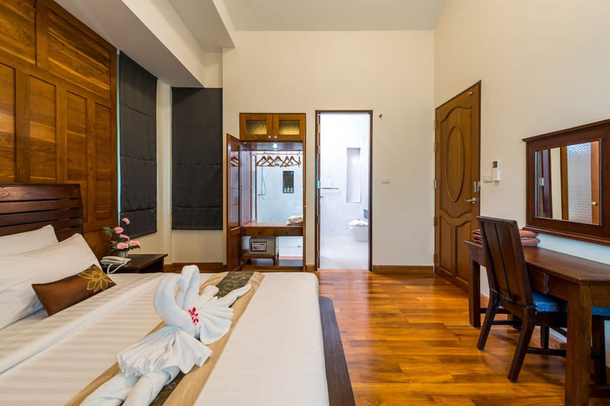 Quarto de hotel com cama grande, cabeceira de madeira, escrivaninha e uma cadeira.