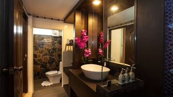 Un baño moderno con pared de piedra, un lavamanos grande blanco y flores rosas.