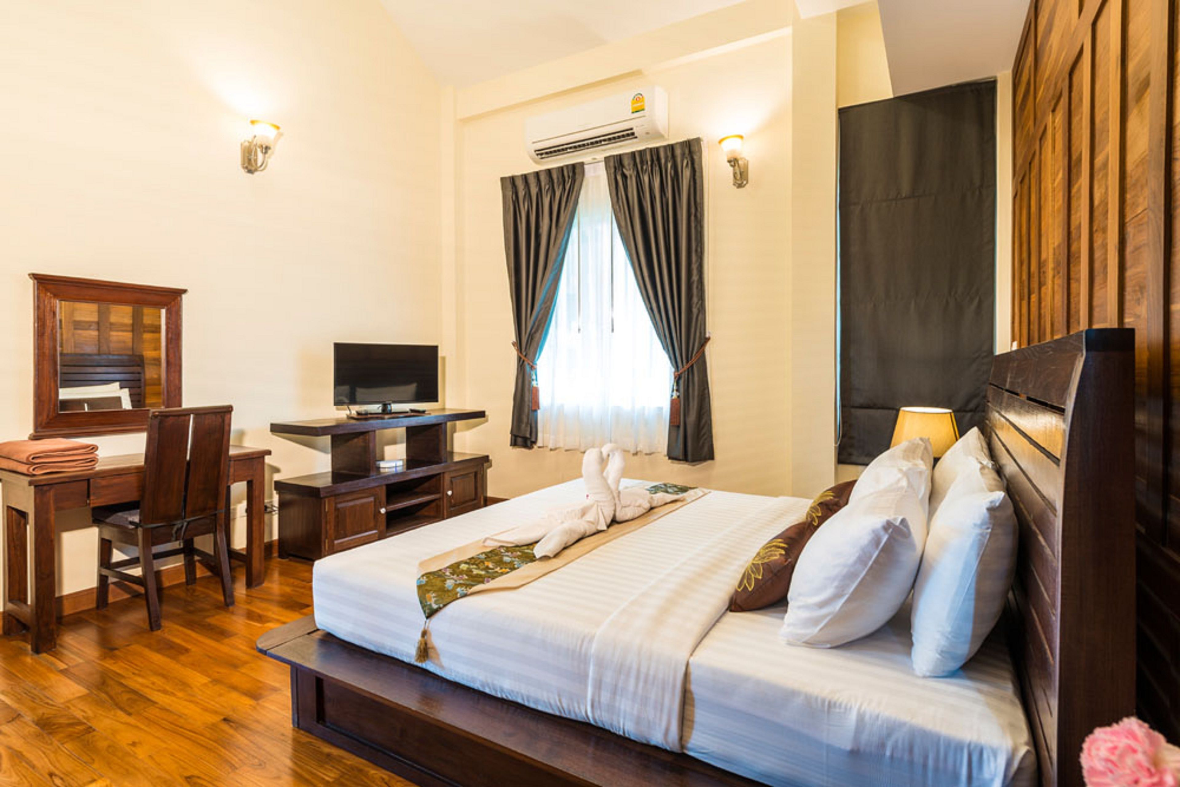 Una habitación de hotel con cama, escritorio, silla, televisión y aire acondicionado.