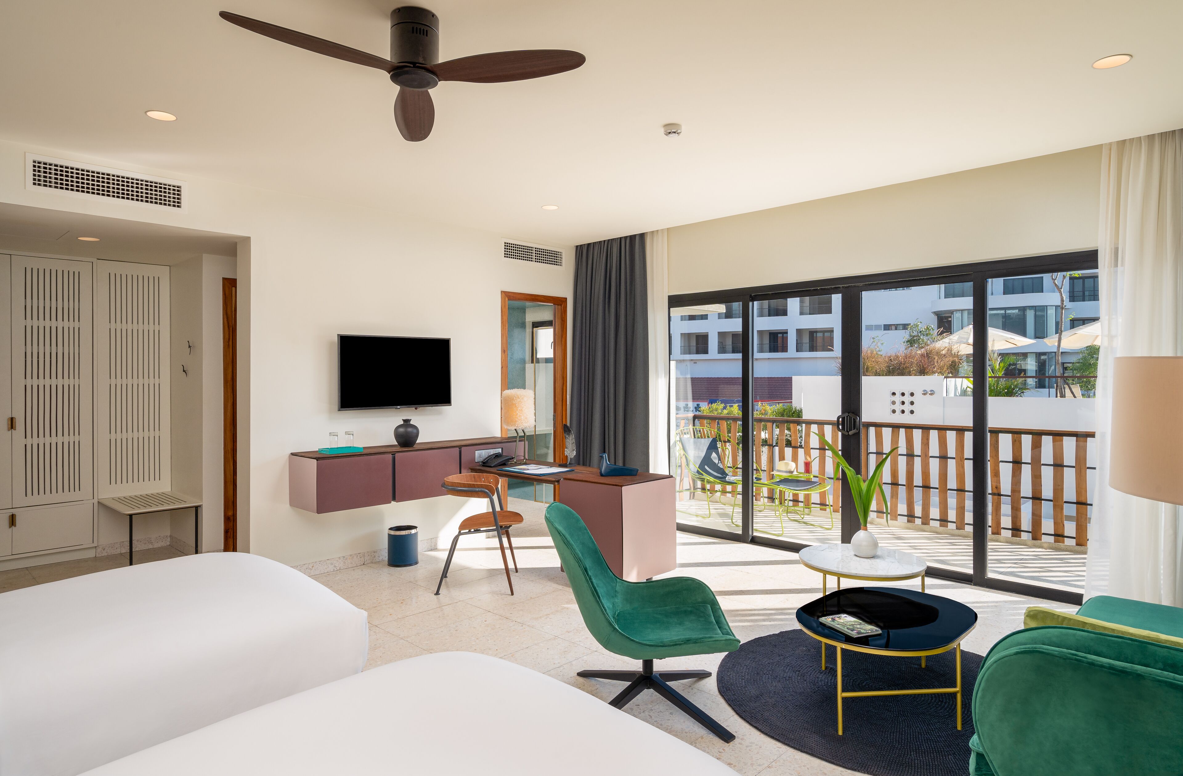 Habitación de hotel moderna con una cama grande, un escritorio con computadora, televisor y balcón con vista a edificios.