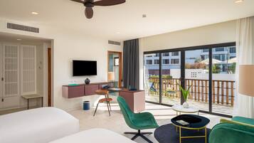 Habitación de hotel moderna con una cama grande, un escritorio con computadora, televisor y balcón con vista a edificios.
