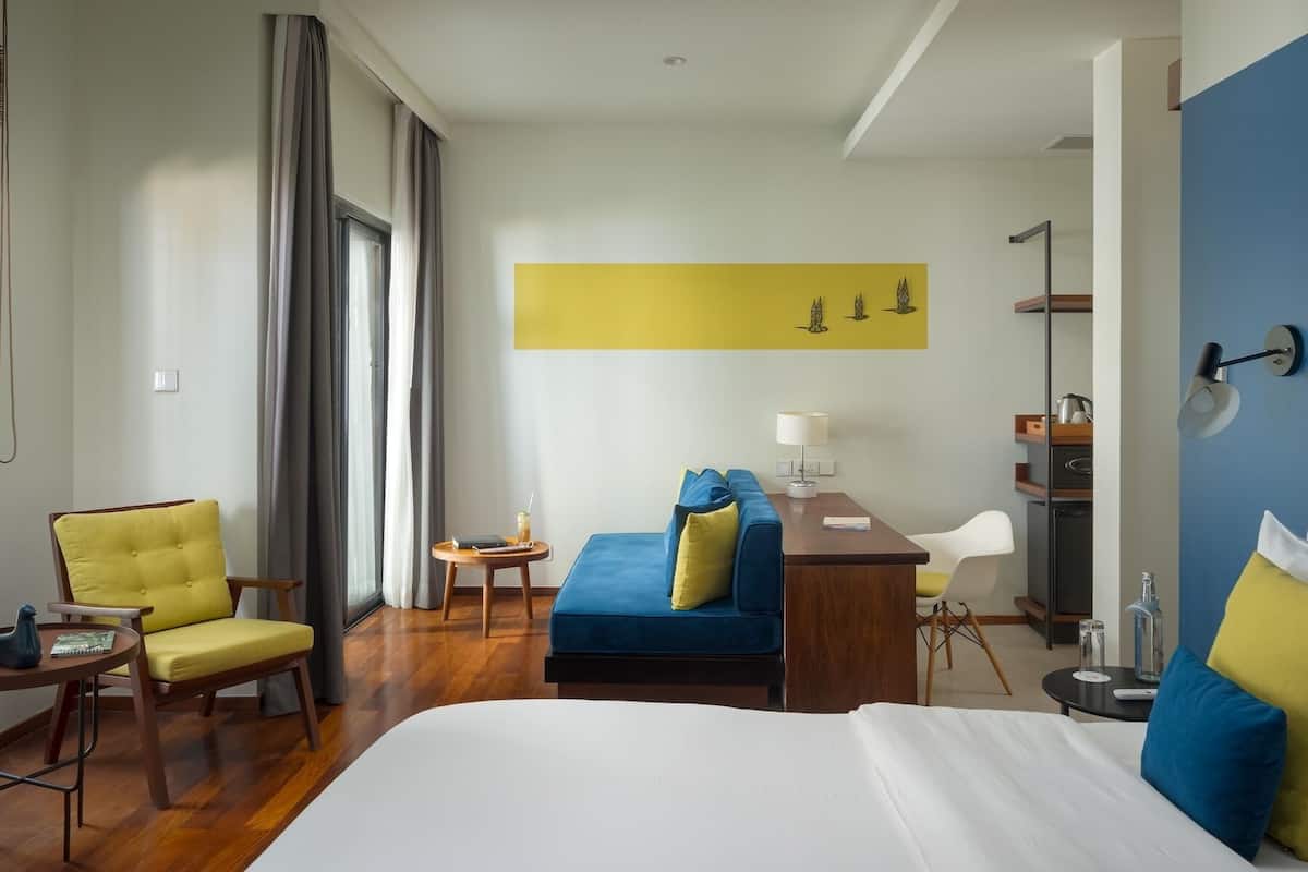 A hotel room with a bed, a desk, a chair, a small table, and a sofa.