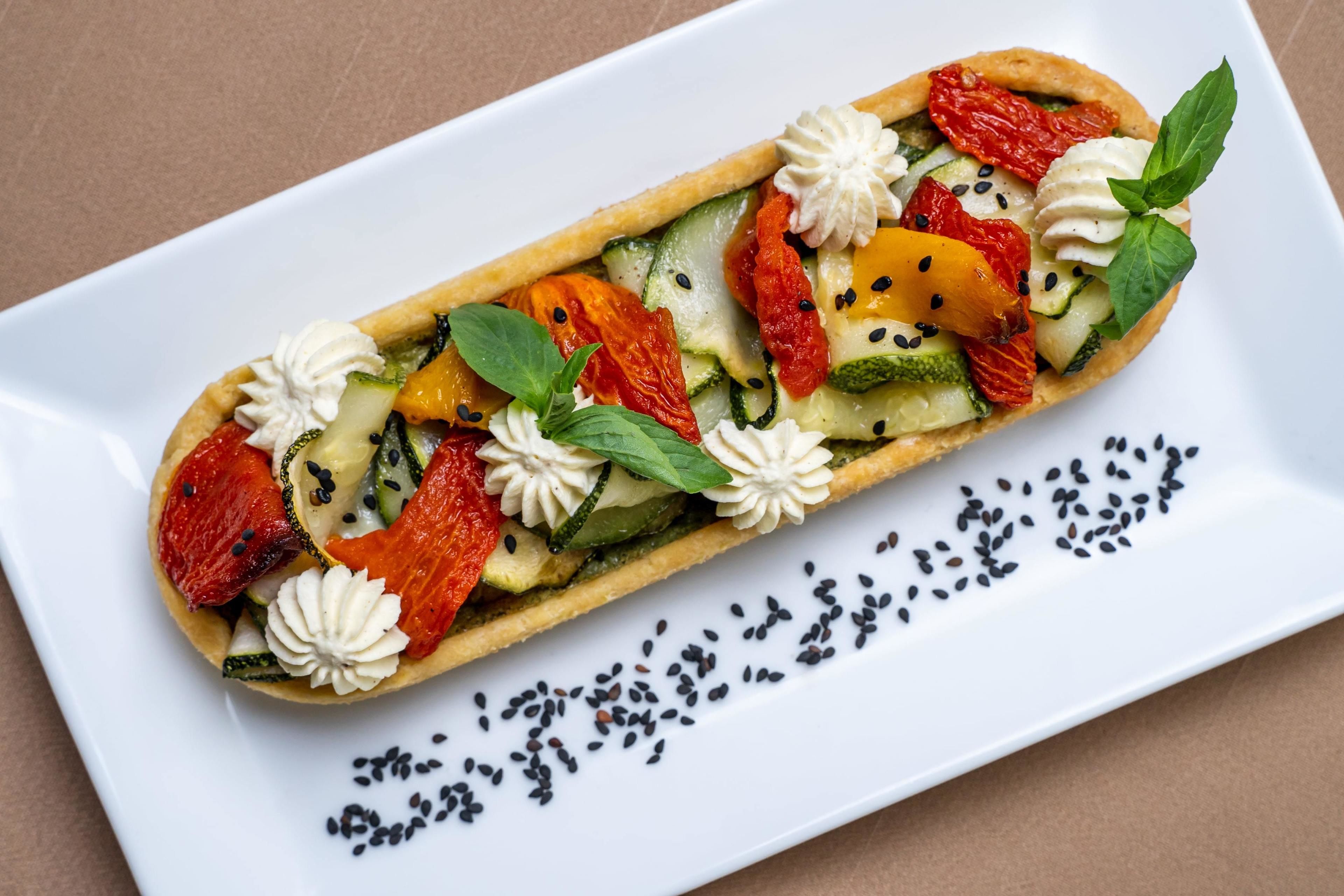 A long, narrow pastry with various vegetables and garnishes on a white plate.