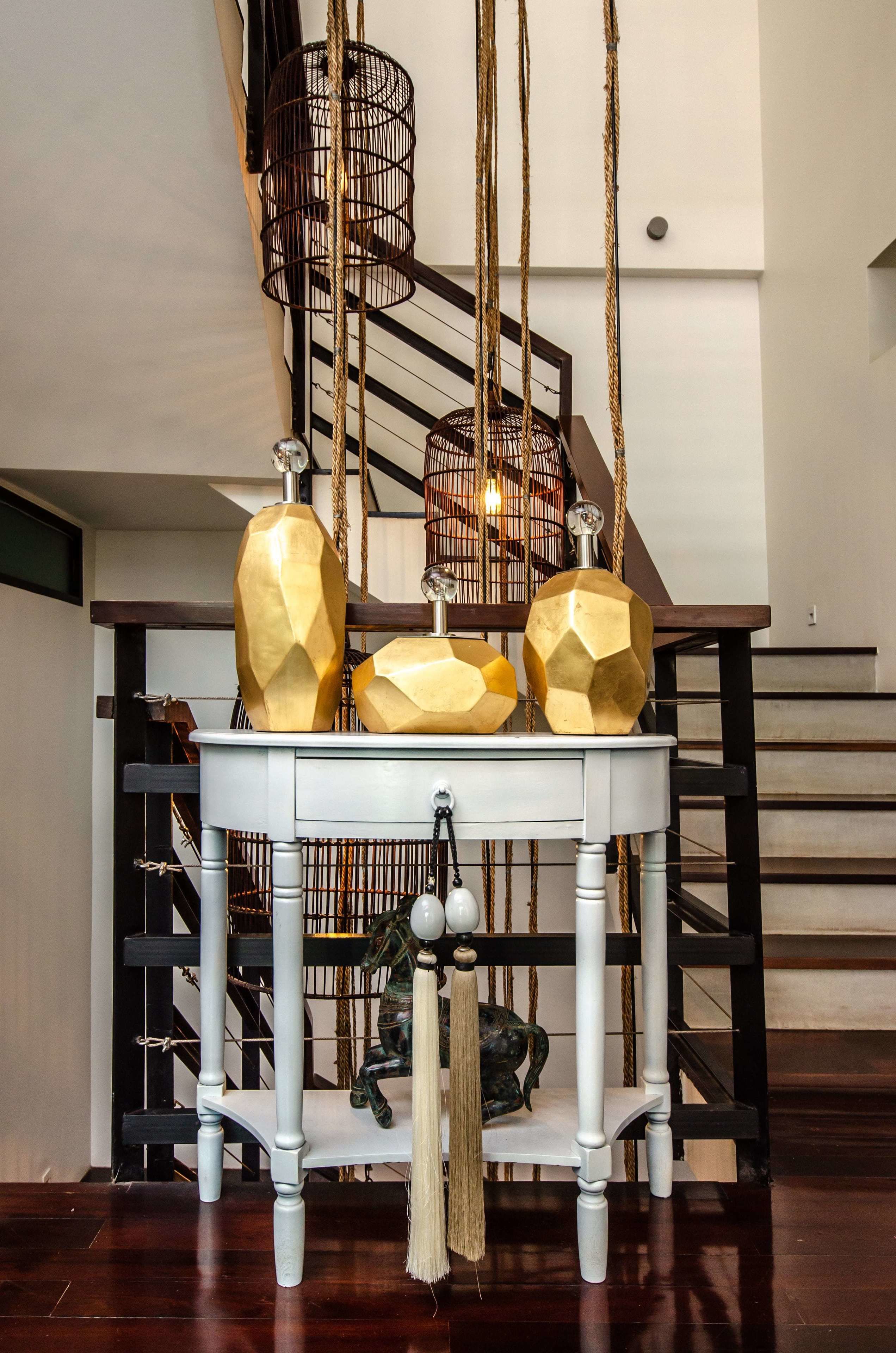 A staircase with a white railing and a table with geometric golden vases and a hanging lantern.