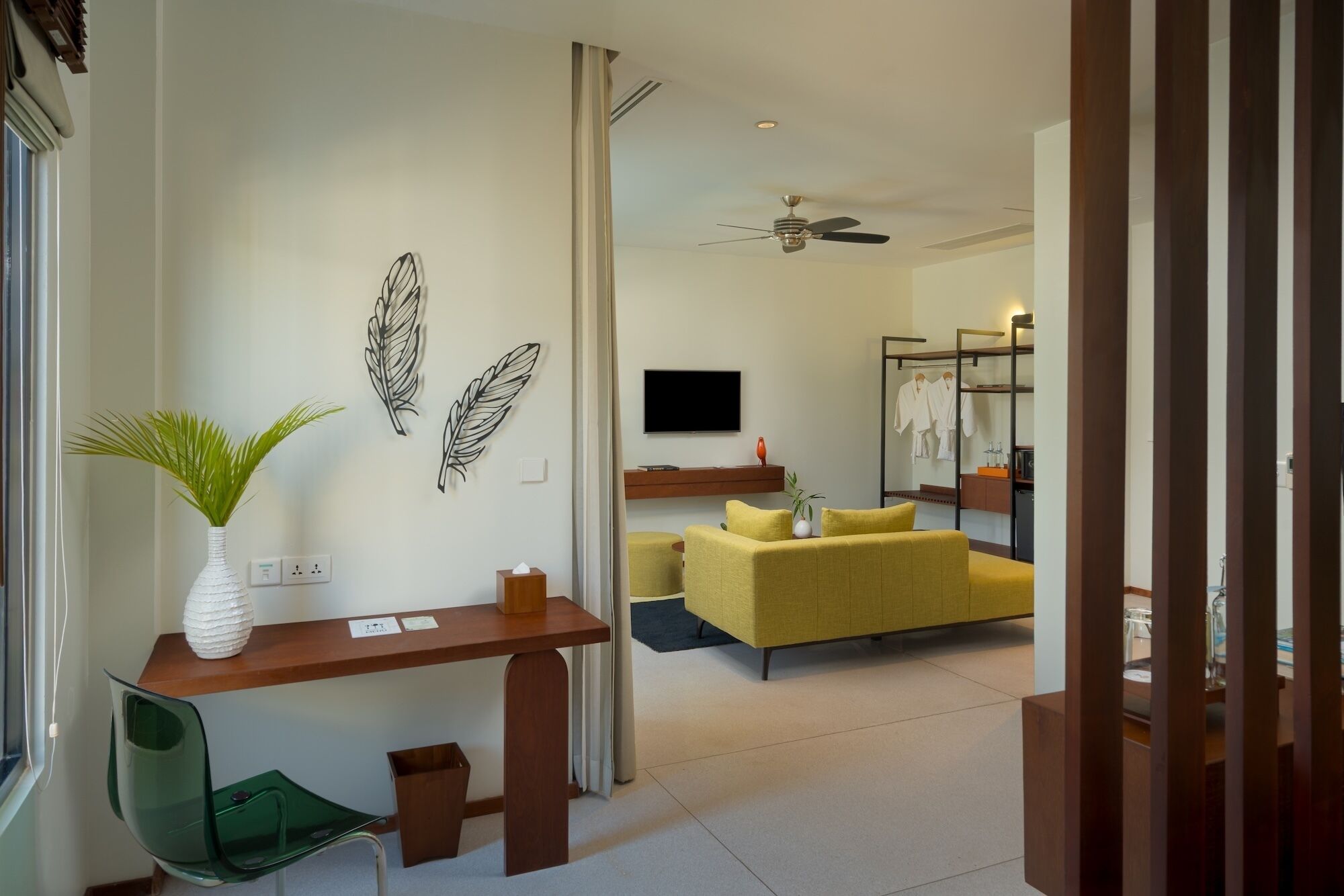 A modern hotel room with a desk, a yellow sofa, a television, and a mirror.