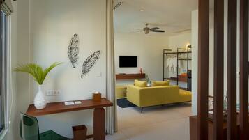 A modern hotel room with a desk, a yellow sofa, a television, and a mirror.