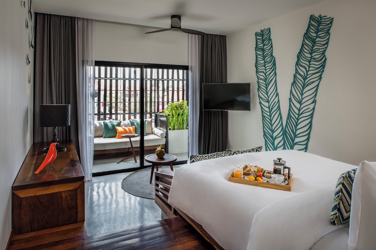A hotel room with a bed, a desk, a TV, and a balcony with a view.