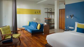 A hotel room with a bed, a blue sofa, a wooden chair, a small table, and a desk with a lamp.