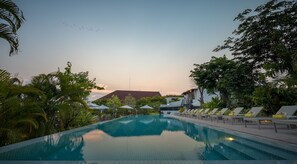 A swimming pool with lounge chairs, surrounded by tropical vegetation and a building in the background. - The Aviary Hotel (Siem Reap)