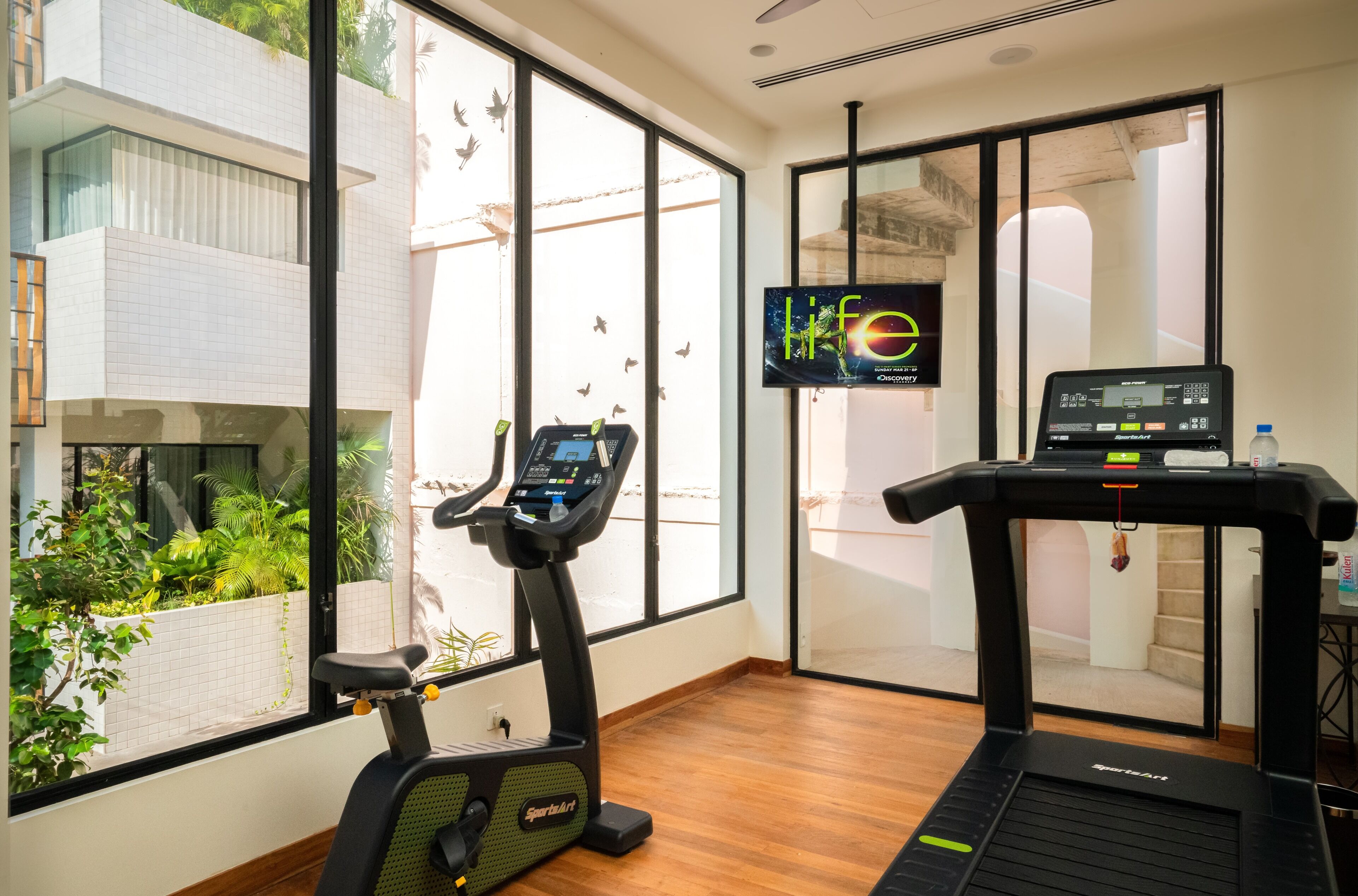 A fitness room with a treadmill, an elliptical, and a TV screen displaying a movie.