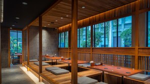 Een modern restaurant met houten tafels en banken, grote ramen en uitzicht op groen.