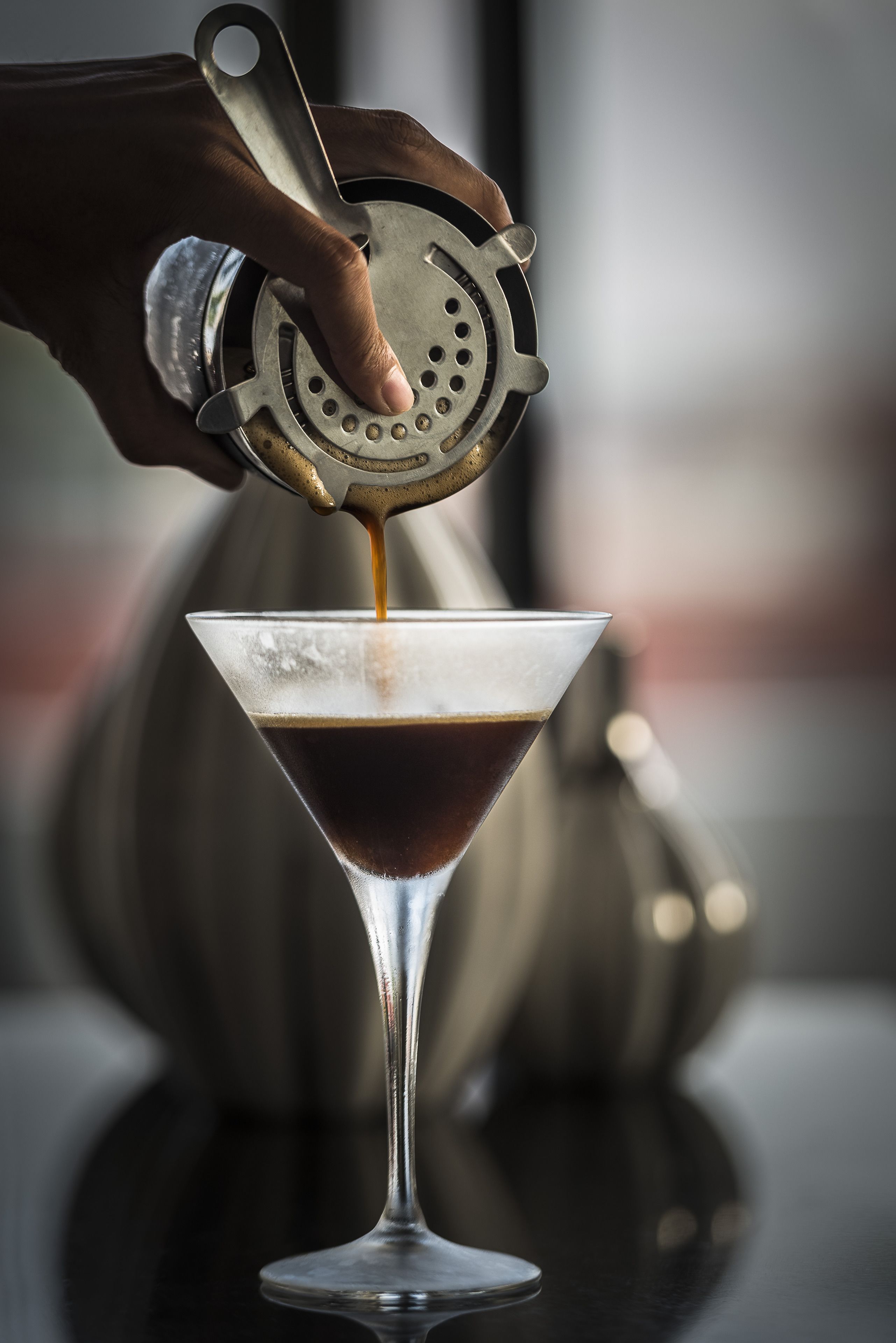 Une main versant une boisson dans un verre à martini.