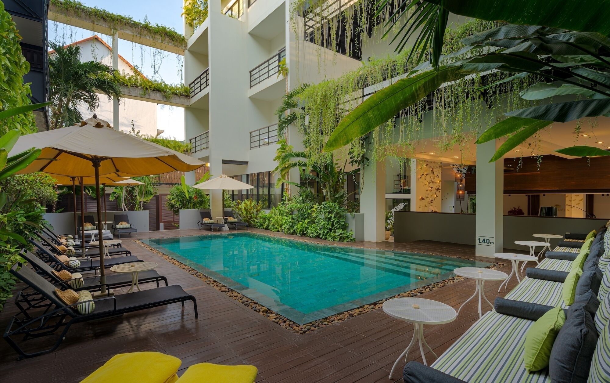 A pool area with lounge chairs, umbrellas, and greenery.