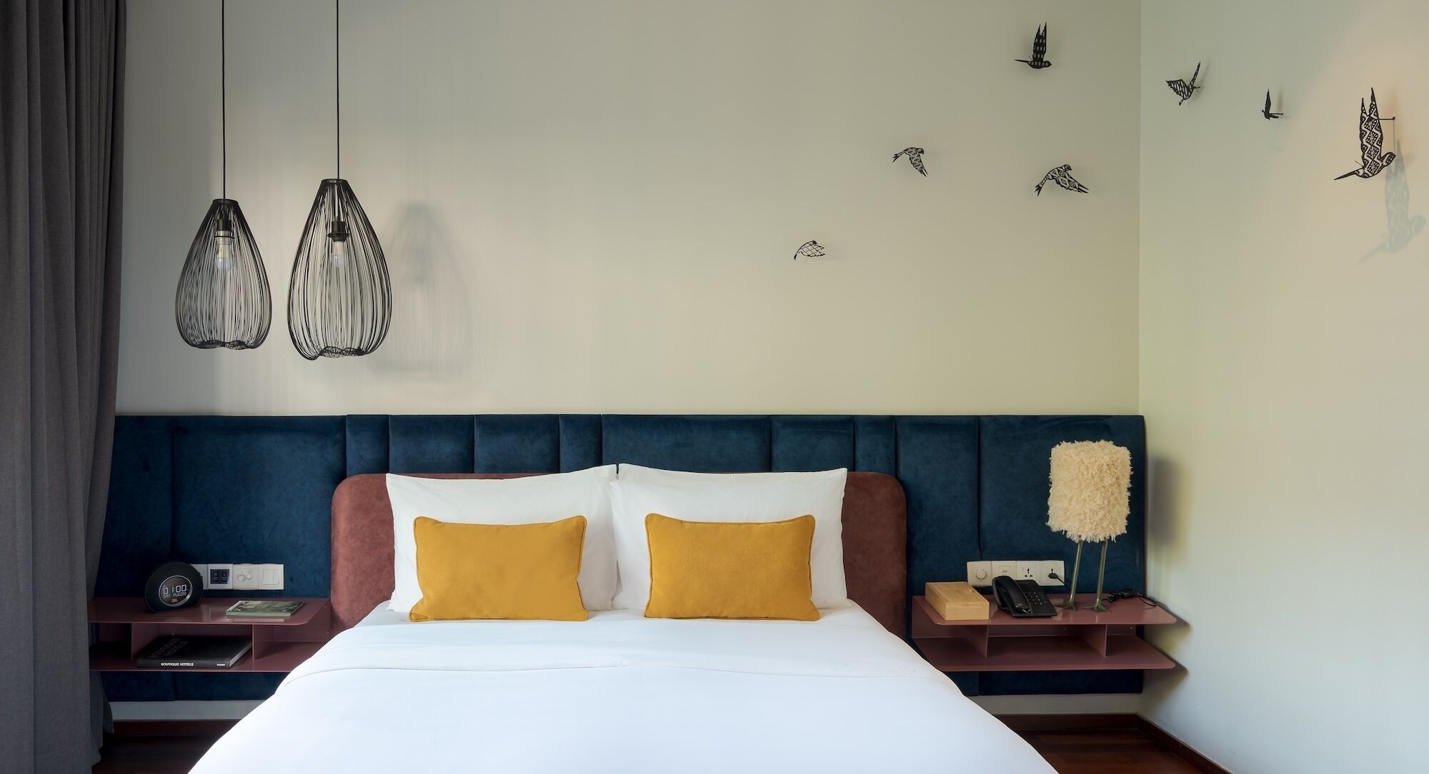 Habitación de hotel con cama, dos mesitas de noche, un reloj de pared, teléfono y decoración en la pared.