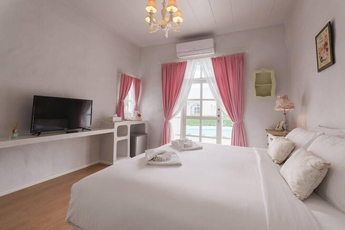 Ein Schlafzimmer mit Bett, Fernseher, Schreibtisch, Stuhl und einem Fenster mit Vorhängen.