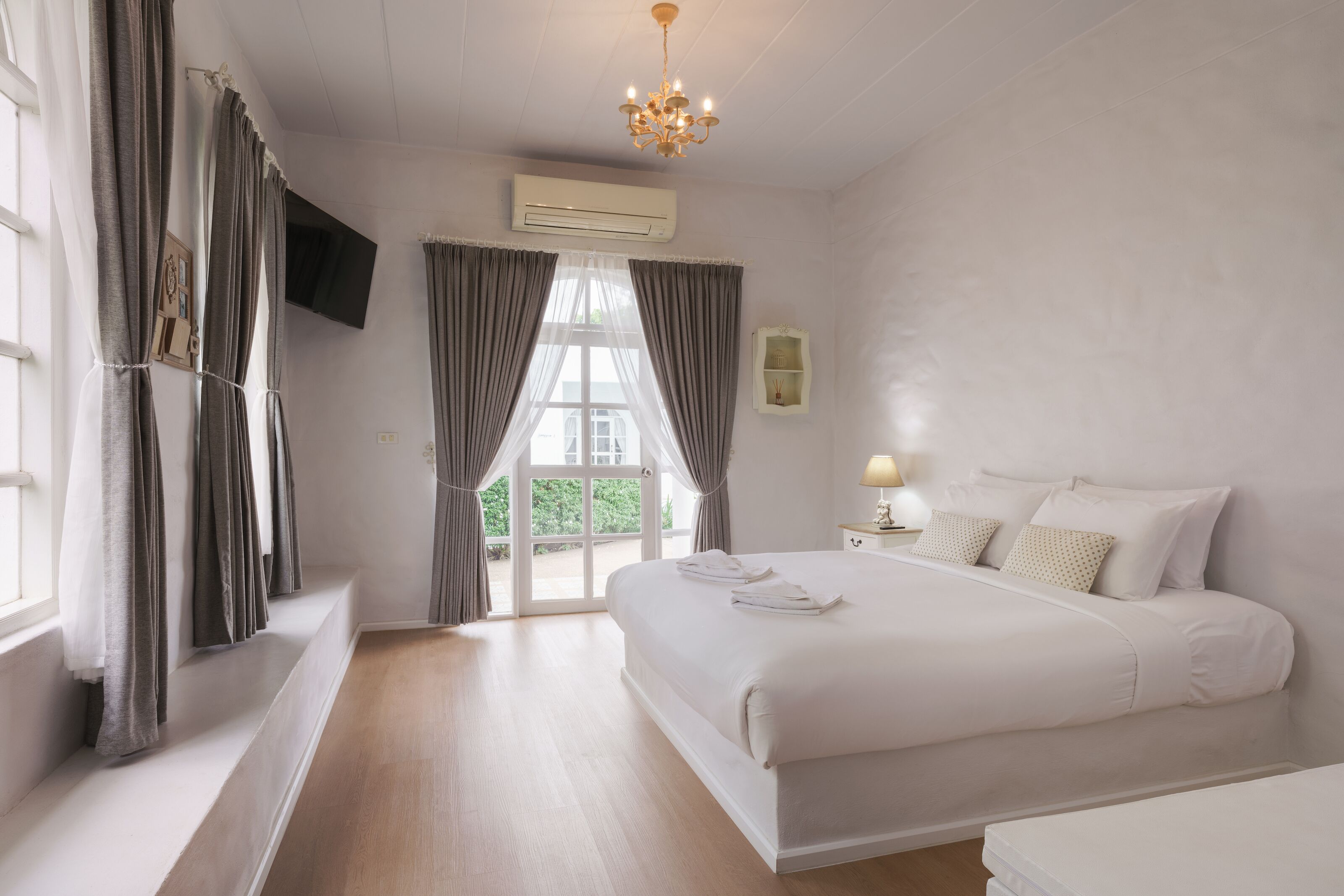 A bedroom with a large bed, a television mounted on the wall, and a window with curtains.