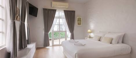 A bedroom with a large bed, a television mounted on the wall, and a window with curtains.