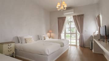 Ein Hotelzimmer mit zwei Betten, einem Schreibtisch mit Computer, einer Lampe und einem großen Fenster mit Vorhängen.