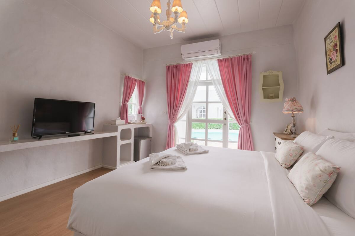 Ein Schlafzimmer mit Bett, Fernseher, Schreibtisch und einem Fenster mit Vorhängen.