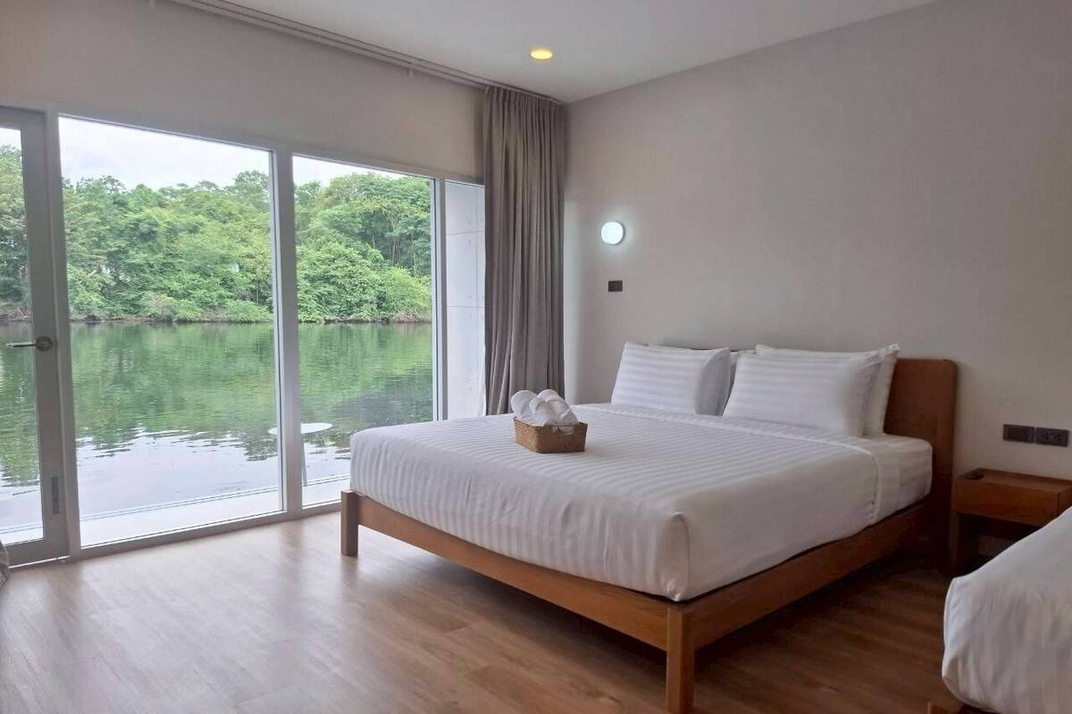 Ein Schlafzimmer mit einem großen Bett, Holzboden, einem Fenster mit Seeblick und einem kleinen Tisch mit einem Korb.