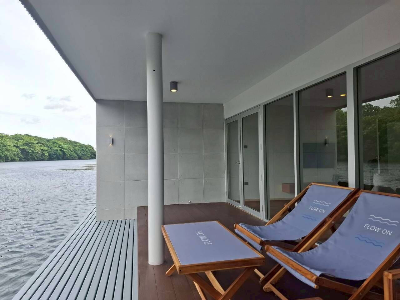 Une terrasse extérieure moderne, dotée de deux chaises longues, d’une grande porte vitrée et offrant une vue sur un lac.