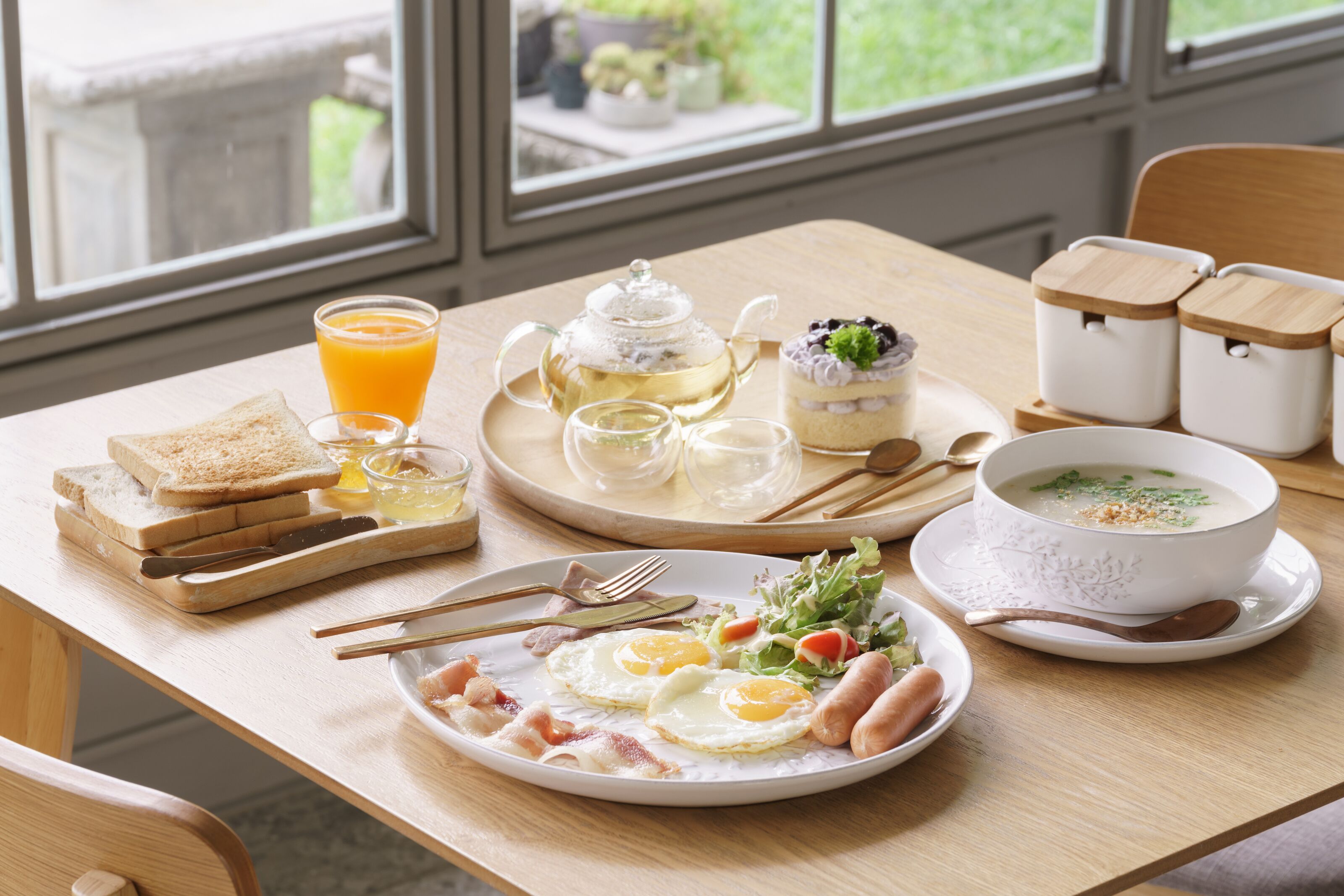 Una mesa de desayuno con tostadas, huevos, salchichas y un tazón de sopa.