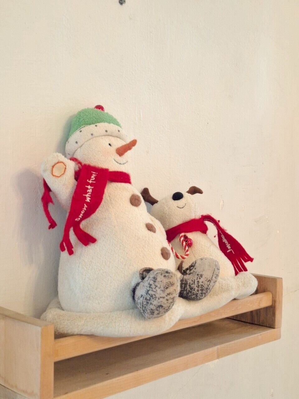 A shelf with two plush toys, one resembling a snowman and the other a dog, both adorned with red scarves.