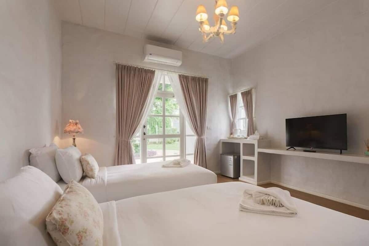 Ein Hotelzimmer mit zwei Betten, einem Fernseher, einem Schreibtisch und einem Fenster mit Vorhängen.