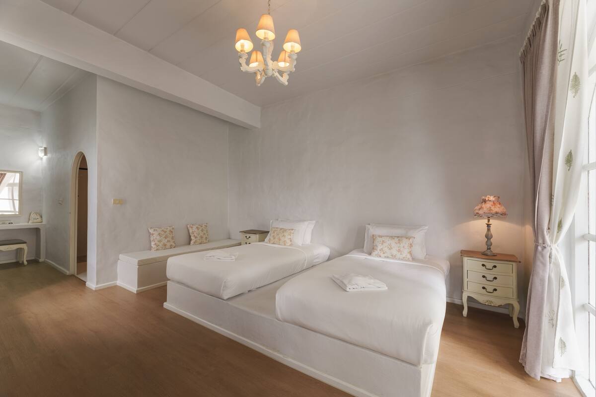 Ein Schlafzimmer mit zwei Betten, einem Nachttisch, einer Lampe und einem Fenster mit Vorhängen.