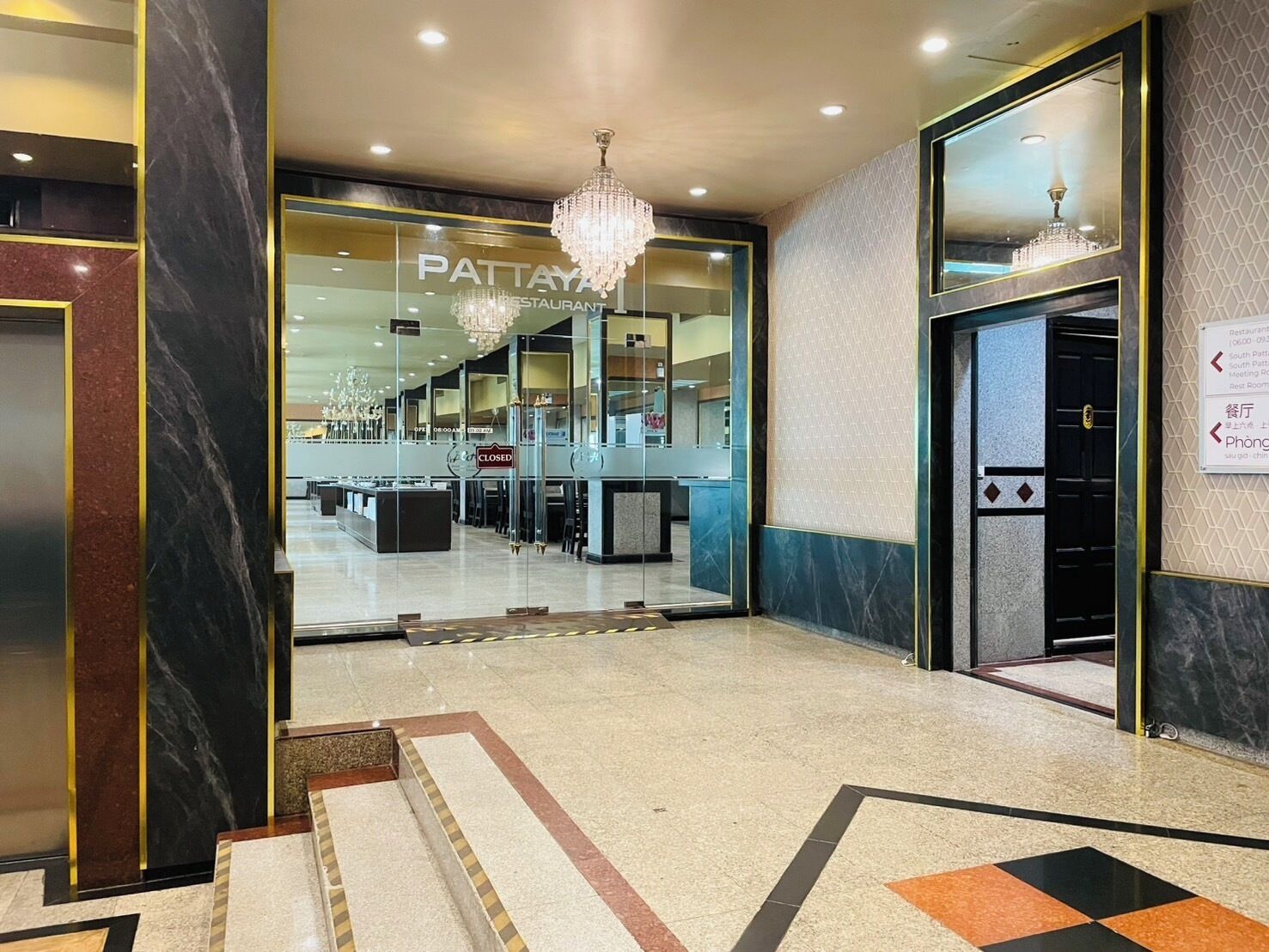 Un hall de hotel con piso de mármol, una araña y un letrero que indica que el restaurante está cerrado.