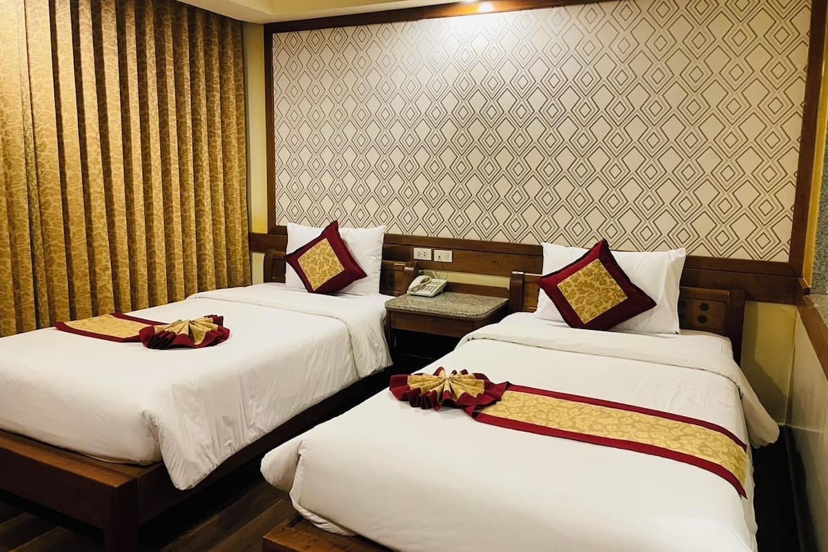 Quarto de hotel com duas camas, cabeceira de madeira, papel de parede estampado e cortina.