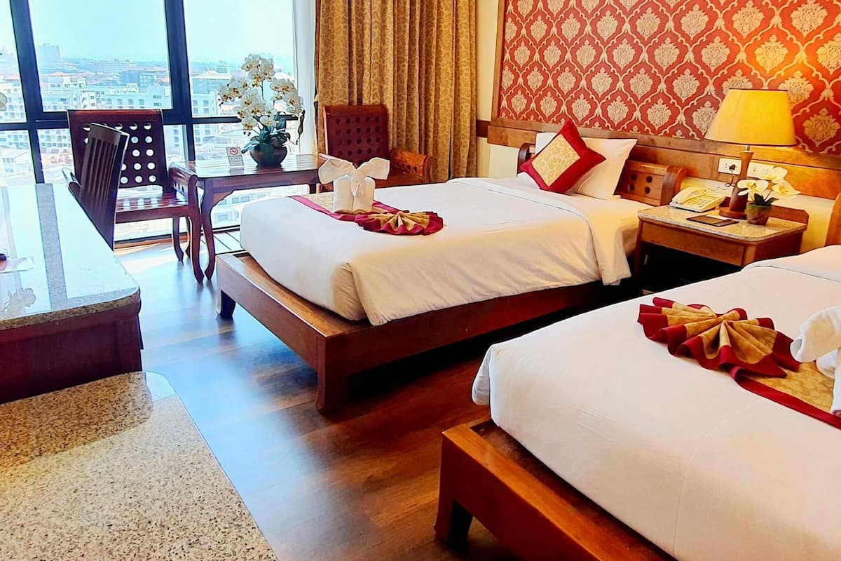 Quarto de hotel com duas camas, uma escrivaninha, uma cadeira, uma mesinha de cabeceira e vista para a cidade.