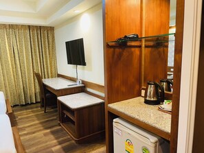 A compact hotel room with a wooden desk, a television, a small refrigerator, and a coffee maker. - Boutique City And Bravo Hotel Pattaya (Pattaya)