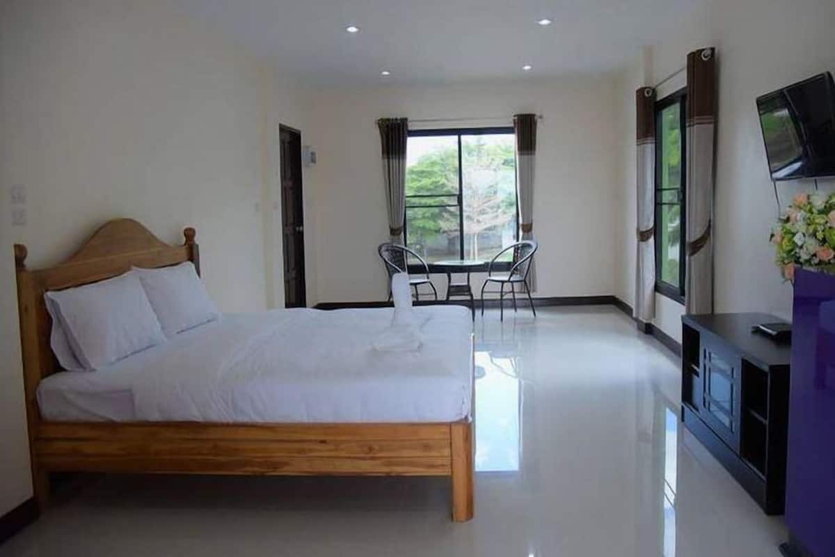 A bedroom with a wooden bed, a small table with chairs, a TV, and a window with curtains.