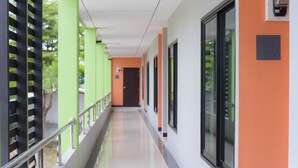 A corridor with green and orange walls, large windows, and a metal railing. - BH Place Apartment (Kanchanaburi)