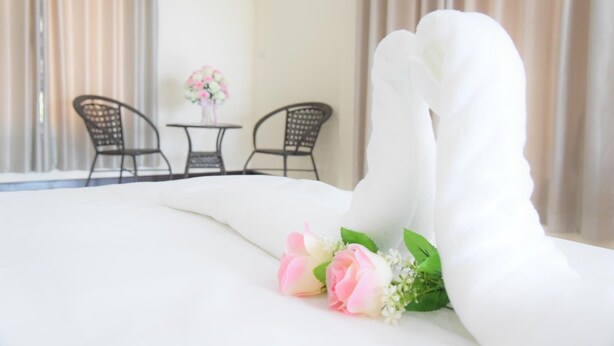 A hotel room with a neatly made bed, a small table with chairs, and a vase of flowers. - BH Place Apartment (Kanchanaburi)