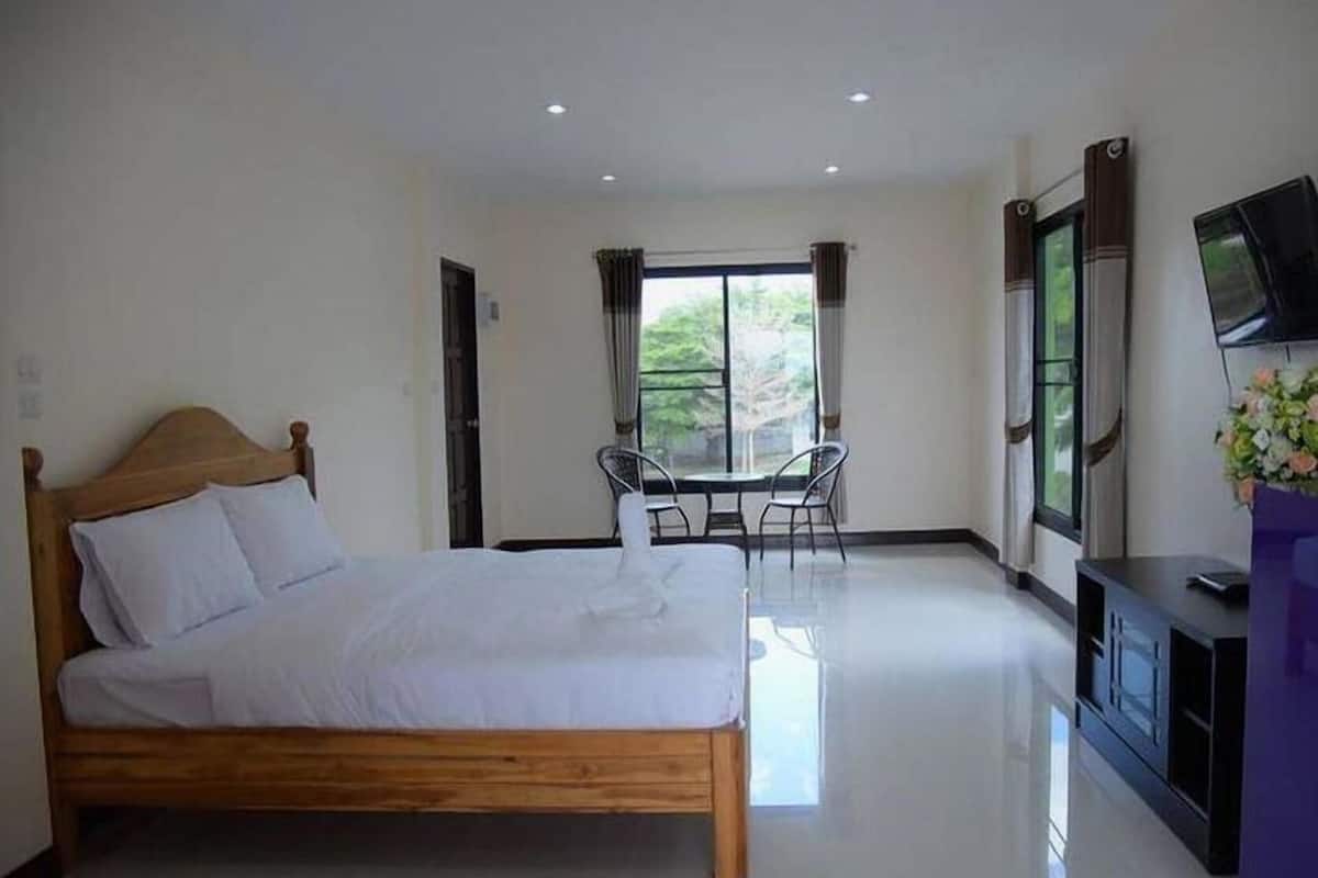 A bedroom with a wooden bed, a small table with chairs, a TV, and a window with curtains.