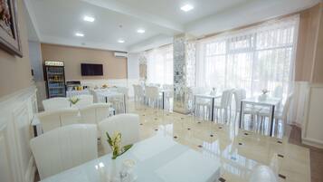 A hotel dining area with white furniture, a refrigerator, and a television on the wall.